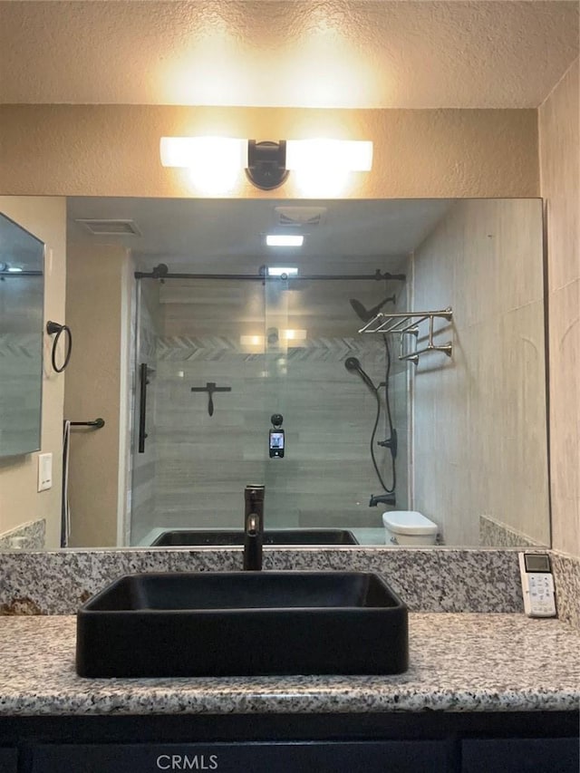 full bath featuring toilet, a stall shower, vanity, and a textured wall