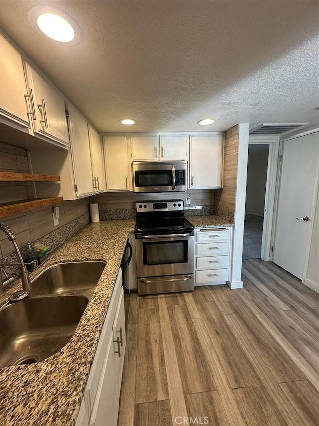 kitchen featuring sink, light hardwood / wood-style flooring, appliances with stainless steel finishes, dark stone counters, and white cabinets