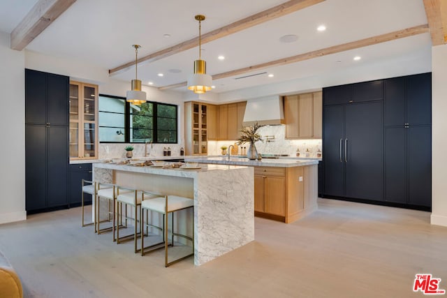 kitchen with light brown cabinetry, hanging light fixtures, a large island, light stone counters, and wall chimney range hood