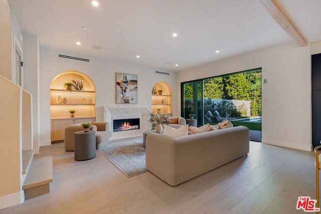 living room with a high end fireplace, light hardwood / wood-style flooring, beamed ceiling, and built in shelves