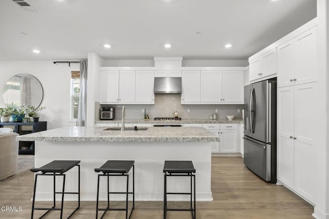 kitchen with sink, light stone counters, appliances with stainless steel finishes, an island with sink, and white cabinets