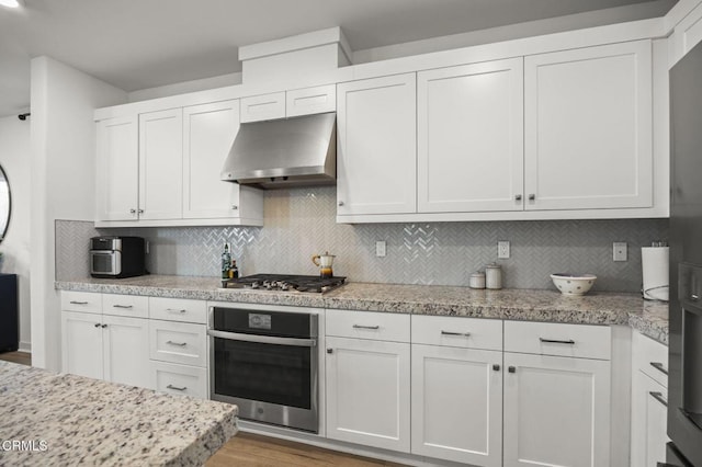 kitchen featuring white cabinetry, appliances with stainless steel finishes, wall chimney range hood, and decorative backsplash