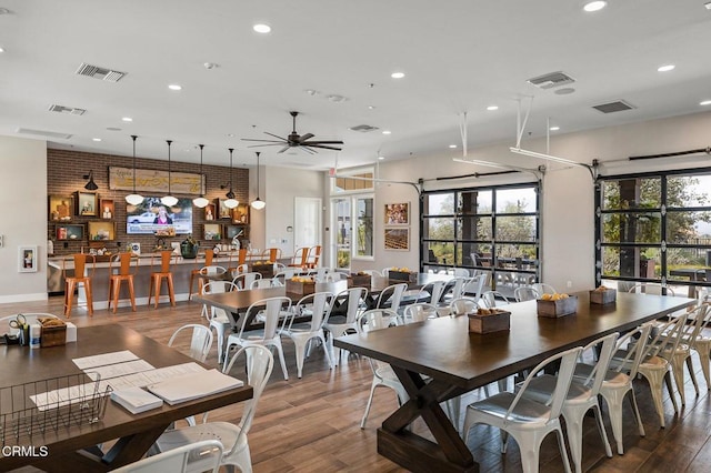 dining area featuring wood-type flooring, brick wall, and ceiling fan