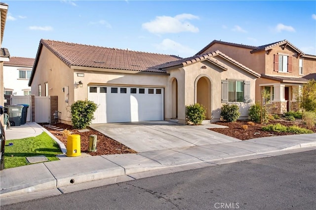 mediterranean / spanish-style home with driveway, an attached garage, a tiled roof, and stucco siding