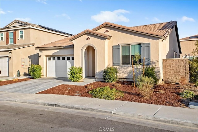 mediterranean / spanish house featuring an attached garage, a tile roof, concrete driveway, and stucco siding