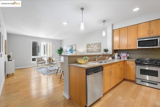 kitchen featuring sink, decorative light fixtures, kitchen peninsula, stainless steel appliances, and light hardwood / wood-style floors