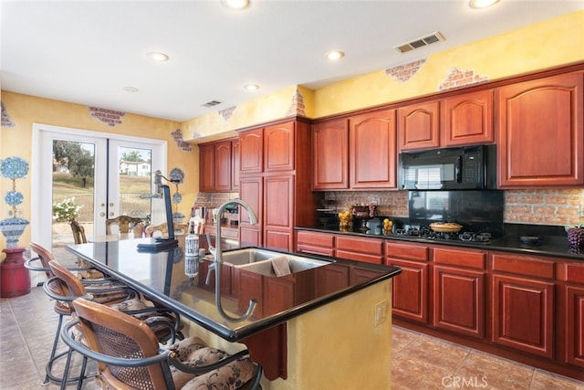 kitchen featuring sink, decorative backsplash, a kitchen island with sink, black appliances, and french doors