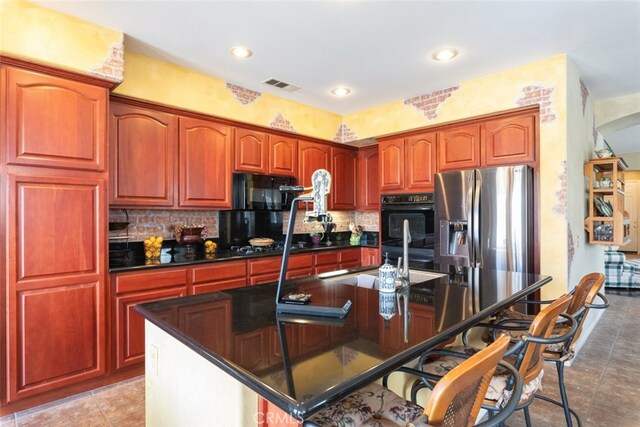 kitchen featuring stainless steel fridge, double oven, a center island with sink, and backsplash