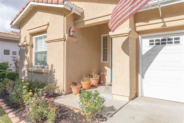 property entrance with stucco siding, a garage, and a tiled roof