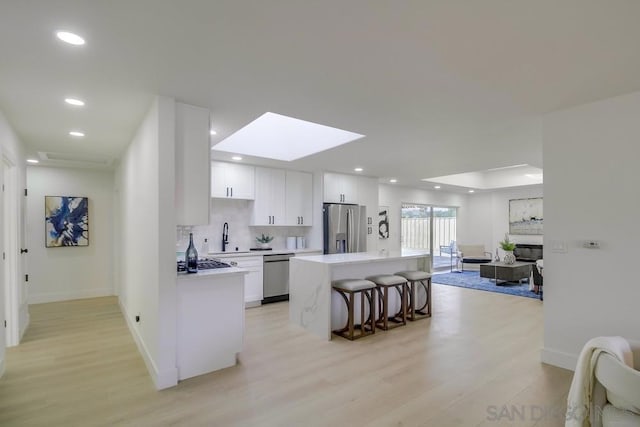 kitchen with a breakfast bar, appliances with stainless steel finishes, white cabinetry, a skylight, and a kitchen island