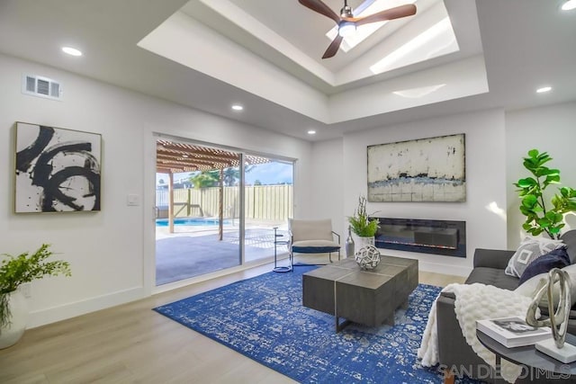 living room with a tray ceiling, wood-type flooring, and ceiling fan