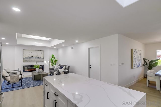 kitchen featuring a skylight, light stone countertops, light hardwood / wood-style floors, and white cabinets