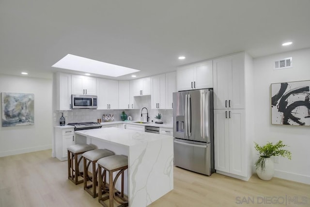 kitchen featuring a skylight, white cabinetry, sink, a center island, and stainless steel appliances