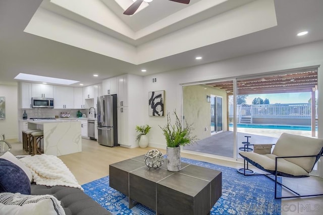 living room with sink, light hardwood / wood-style flooring, a raised ceiling, and ceiling fan