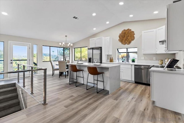 kitchen featuring vaulted ceiling, a kitchen island, pendant lighting, white cabinets, and stainless steel appliances