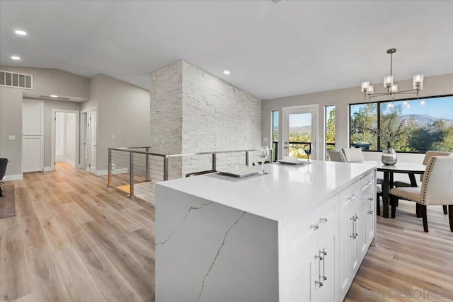 kitchen with hanging light fixtures, an island with sink, white cabinets, and light hardwood / wood-style flooring