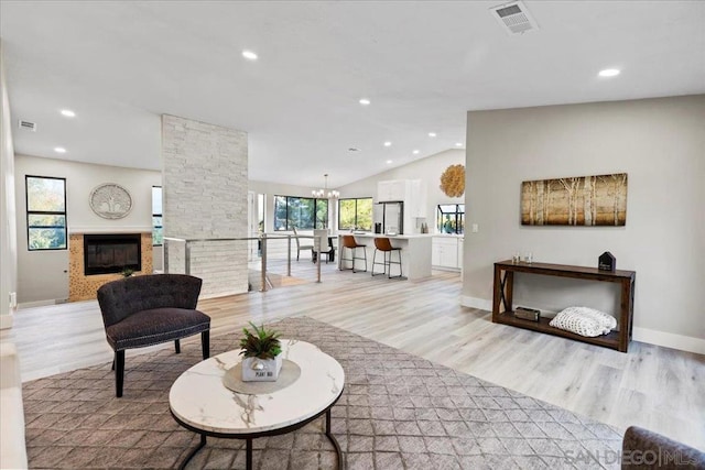 living room featuring lofted ceiling, a stone fireplace, a chandelier, and light wood-type flooring