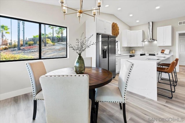 dining area with an inviting chandelier, lofted ceiling, sink, and light wood-type flooring