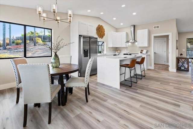 dining space with vaulted ceiling, sink, an inviting chandelier, and light wood-type flooring