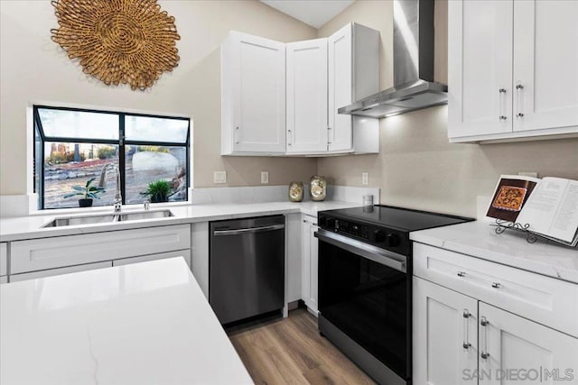 kitchen featuring electric stove, sink, white cabinetry, stainless steel dishwasher, and wall chimney exhaust hood