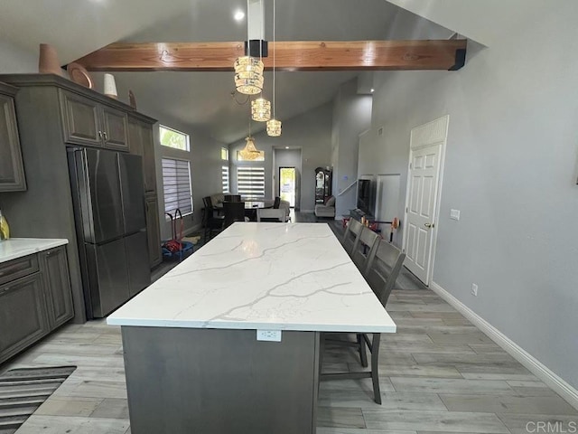 kitchen featuring a kitchen bar, a center island, hanging light fixtures, stainless steel refrigerator, and beamed ceiling