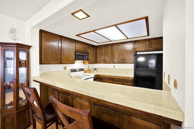 kitchen featuring kitchen peninsula, tile counters, a kitchen breakfast bar, and black appliances