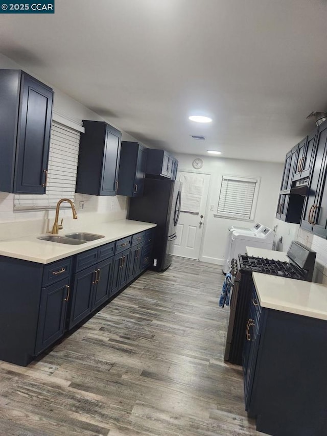 kitchen with washer and clothes dryer, sink, hardwood / wood-style floors, and stainless steel gas stove