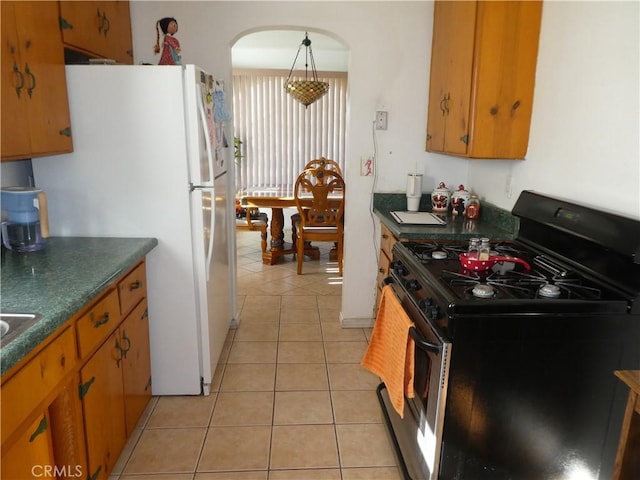 kitchen featuring gas range, decorative light fixtures, light tile patterned flooring, and white fridge