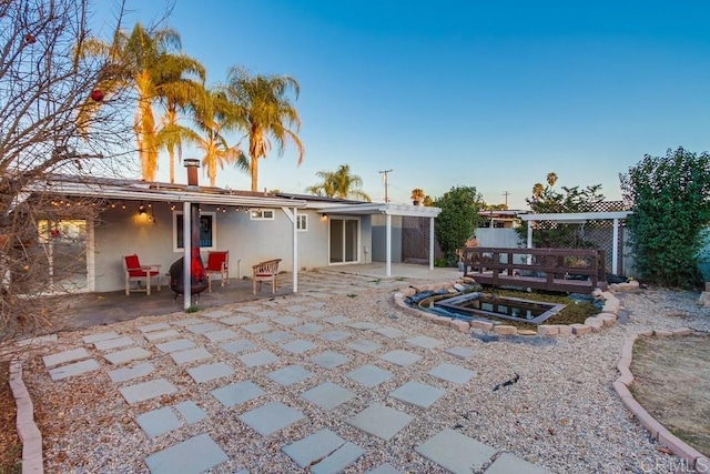 rear view of property with stucco siding, a patio, and an in ground hot tub