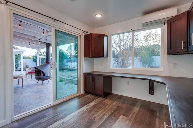 kitchen featuring dark wood-type flooring, dark brown cabinets, a wall mounted AC, built in study area, and dark countertops