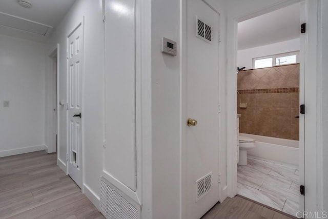 hall with wood finish floors, visible vents, and baseboards