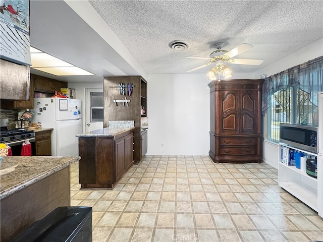 kitchen with dark brown cabinetry, light stone countertops, appliances with stainless steel finishes, and ceiling fan