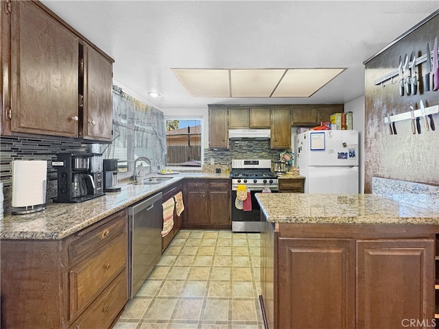 kitchen with sink, backsplash, stainless steel appliances, light stone counters, and dark brown cabinetry