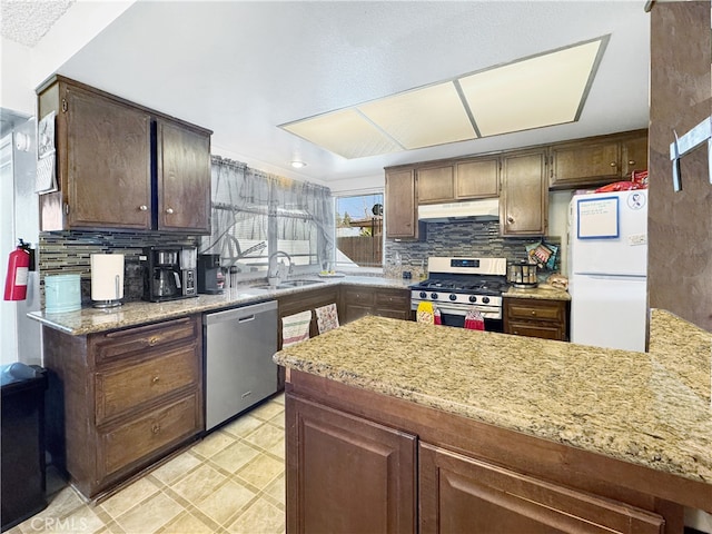 kitchen featuring stainless steel appliances, light stone countertops, sink, and dark brown cabinets