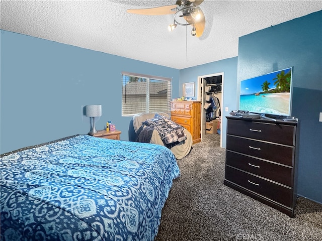 bedroom featuring dark colored carpet, a walk in closet, a textured ceiling, a closet, and ceiling fan