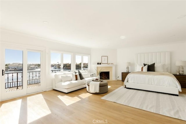 bedroom featuring crown molding, access to exterior, a premium fireplace, a water view, and light hardwood / wood-style flooring