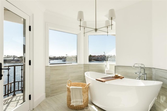 bathroom with a water view, a bath, a chandelier, and tile walls