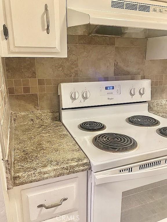 interior details featuring white electric stove, light stone countertops, and white cabinets