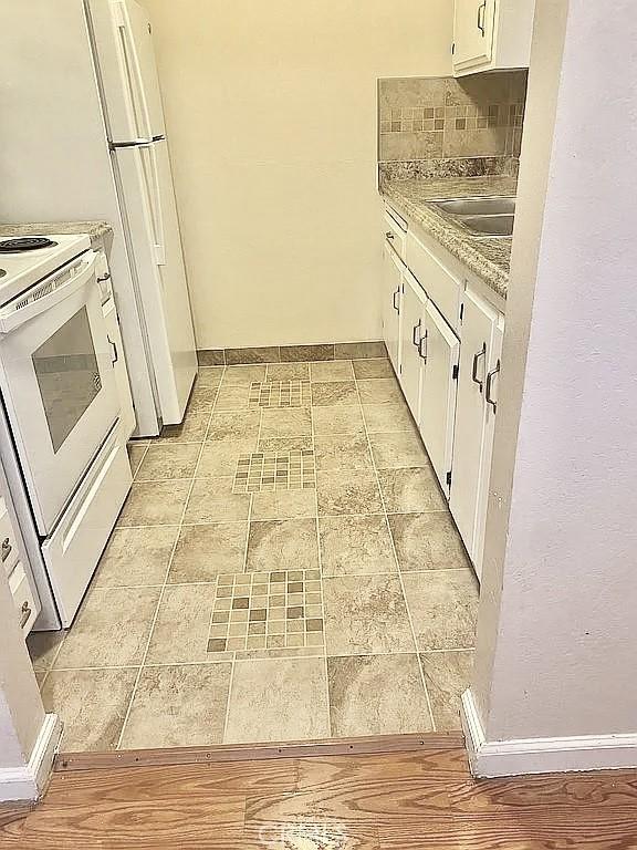 kitchen featuring tasteful backsplash, white cabinetry, white electric stove, sink, and light stone counters