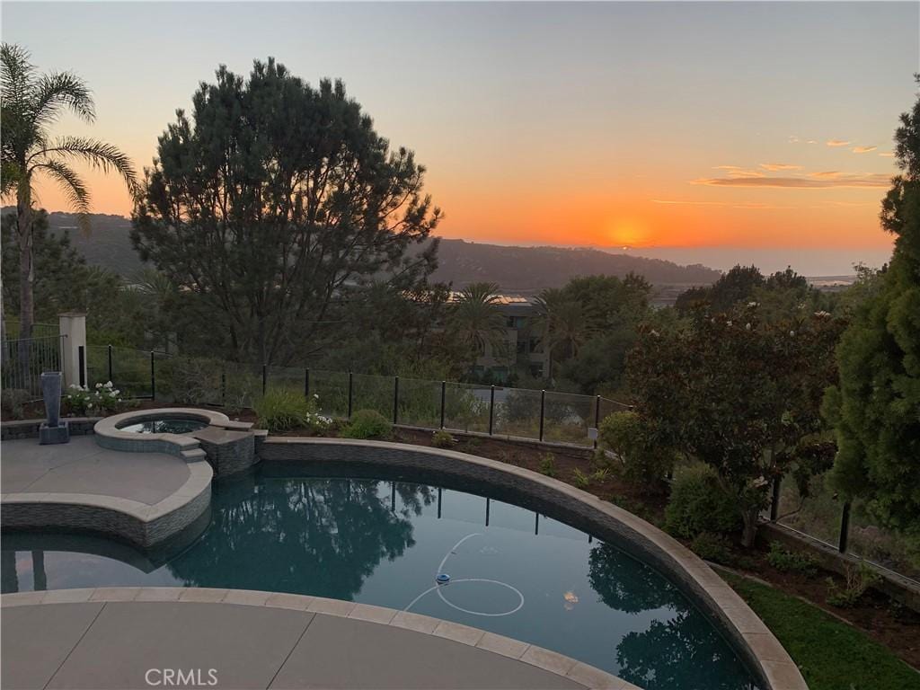 pool at dusk featuring an in ground hot tub