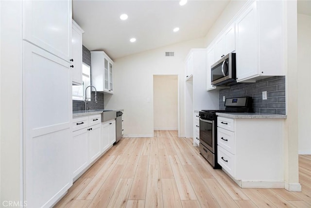 kitchen with vaulted ceiling, light hardwood / wood-style flooring, white cabinets, stainless steel appliances, and backsplash