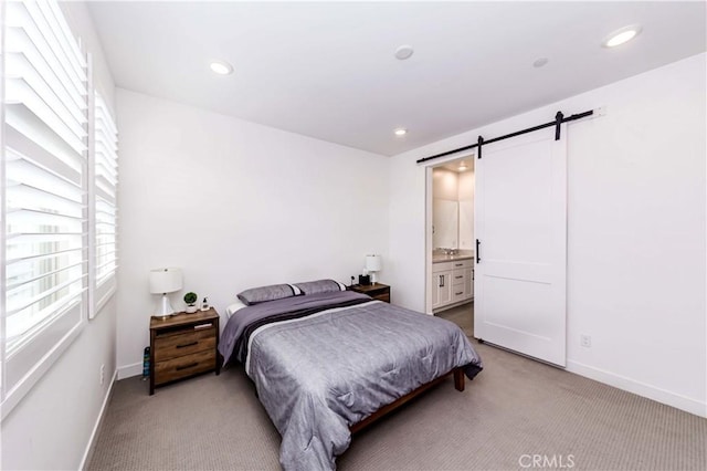 bedroom featuring a barn door, connected bathroom, and light colored carpet