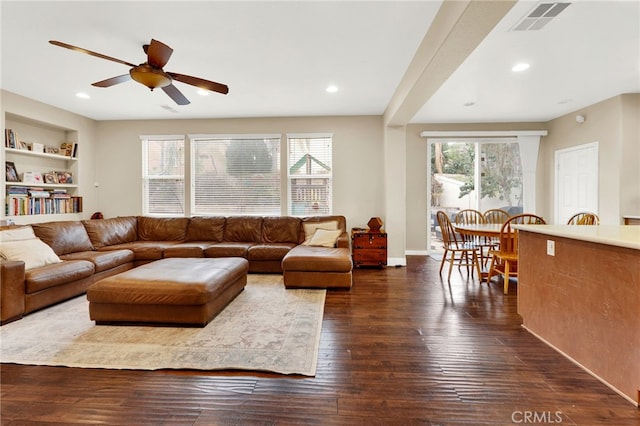 living room featuring built in shelves, ceiling fan, and dark hardwood / wood-style flooring