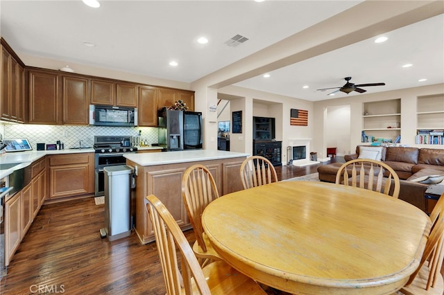 kitchen with dark wood-type flooring, ceiling fan, appliances with stainless steel finishes, a center island, and tasteful backsplash