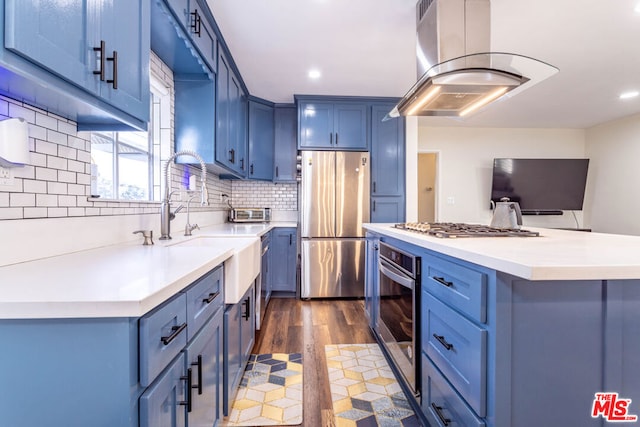 kitchen featuring blue cabinetry, appliances with stainless steel finishes, tasteful backsplash, island exhaust hood, and dark hardwood / wood-style flooring