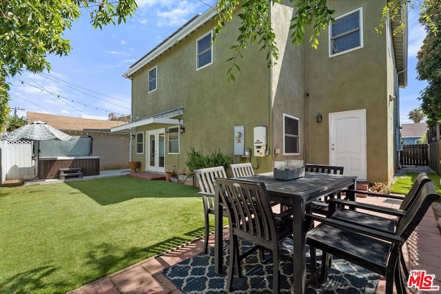 back of house with a patio, a hot tub, and a lawn