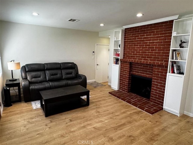 living room featuring built in shelves, a fireplace, and light wood-type flooring