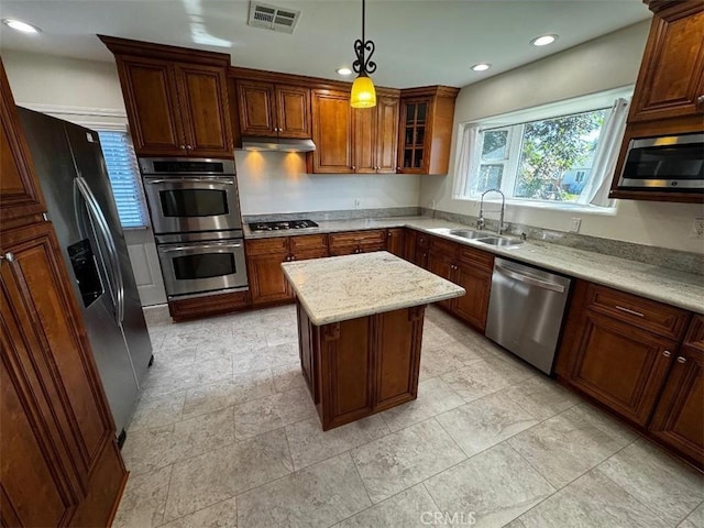 kitchen with appliances with stainless steel finishes, pendant lighting, sink, a center island, and light stone countertops