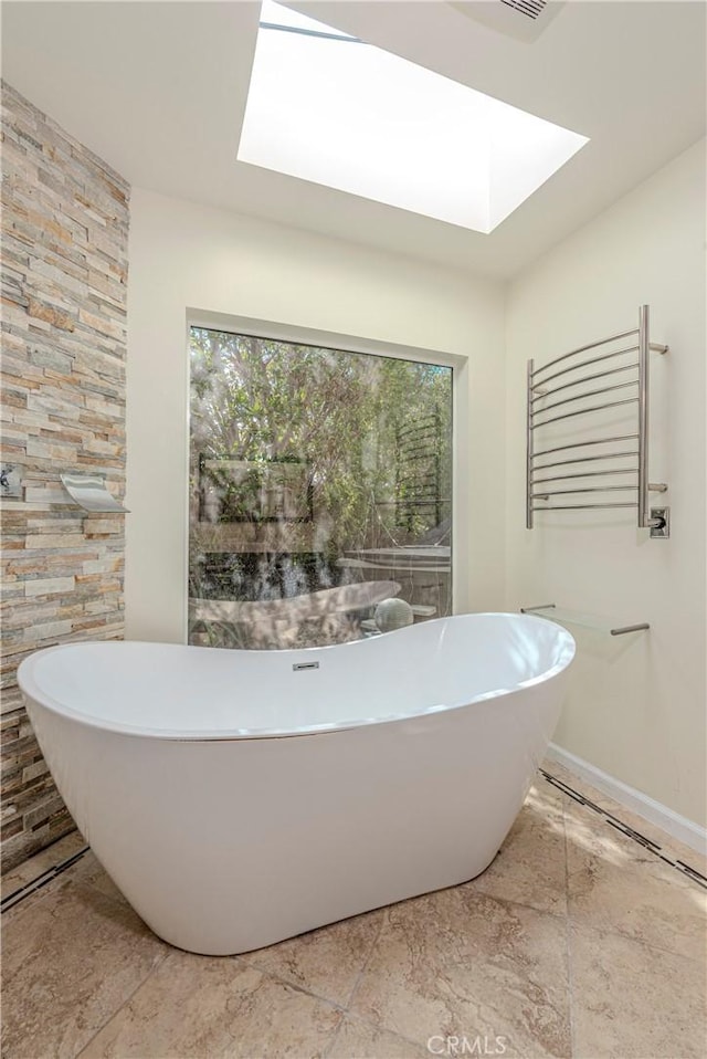 bathroom with a skylight, radiator, a freestanding bath, and baseboards