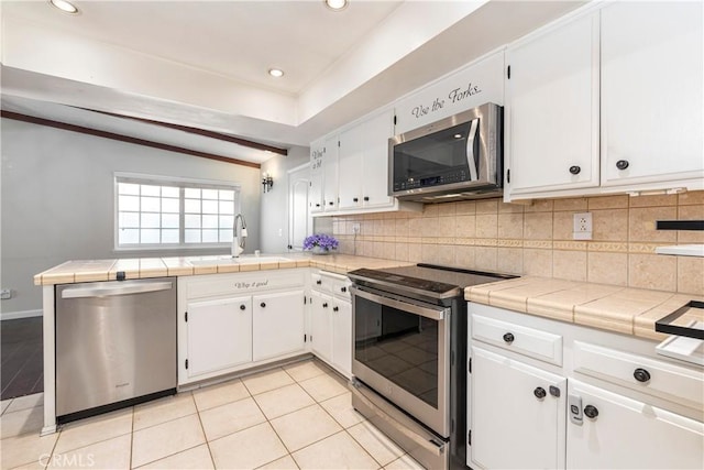 kitchen with stainless steel appliances, a sink, white cabinets, backsplash, and tile counters